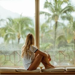 Girl sitting on the bench by the window overlooking palm trees