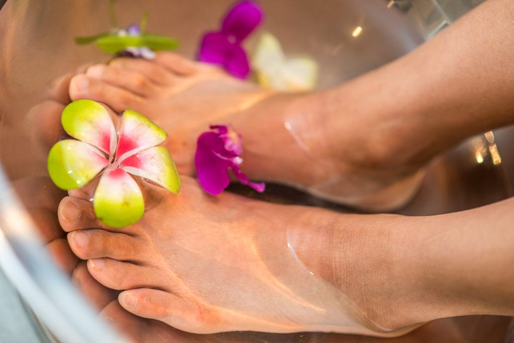 Feet in a bowl with water and frangipani flowers