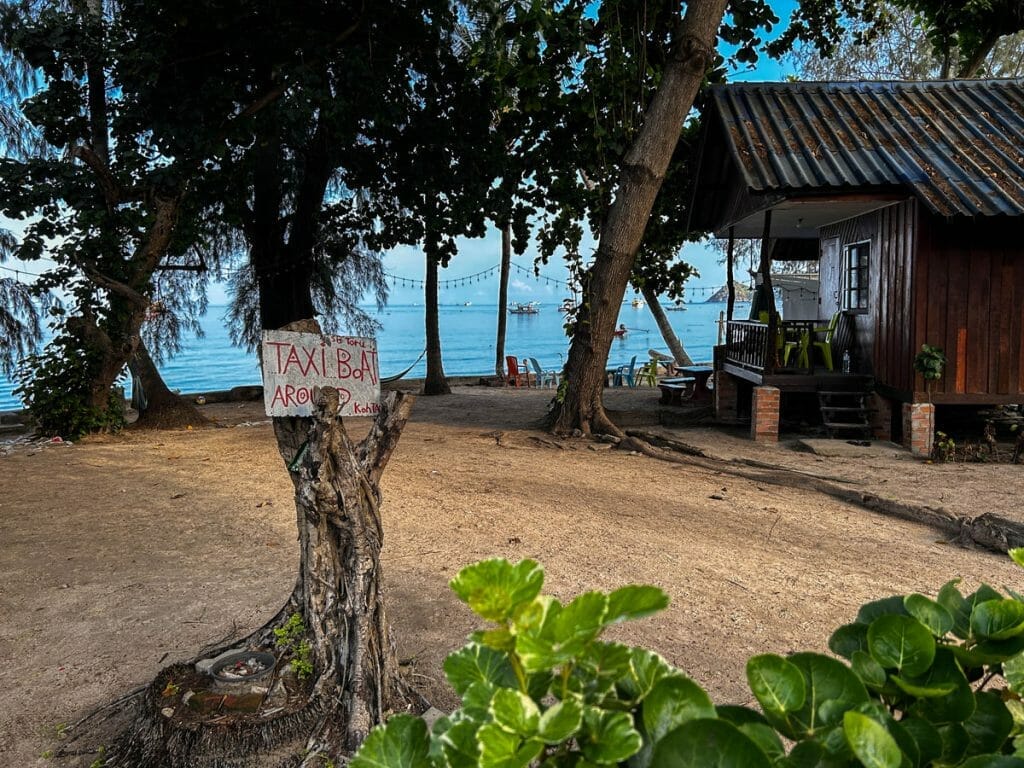 Beach front in Koh Tao with a tree tunk and a sign for taxi boats