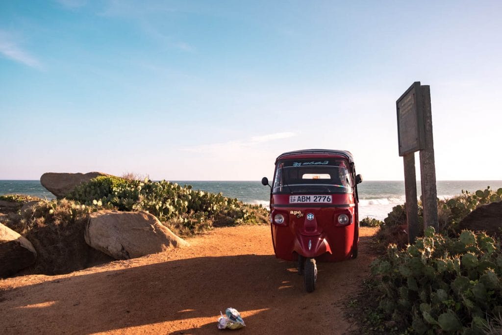 Red tuk-tuk parked at a viewpoint overlooking the ocean