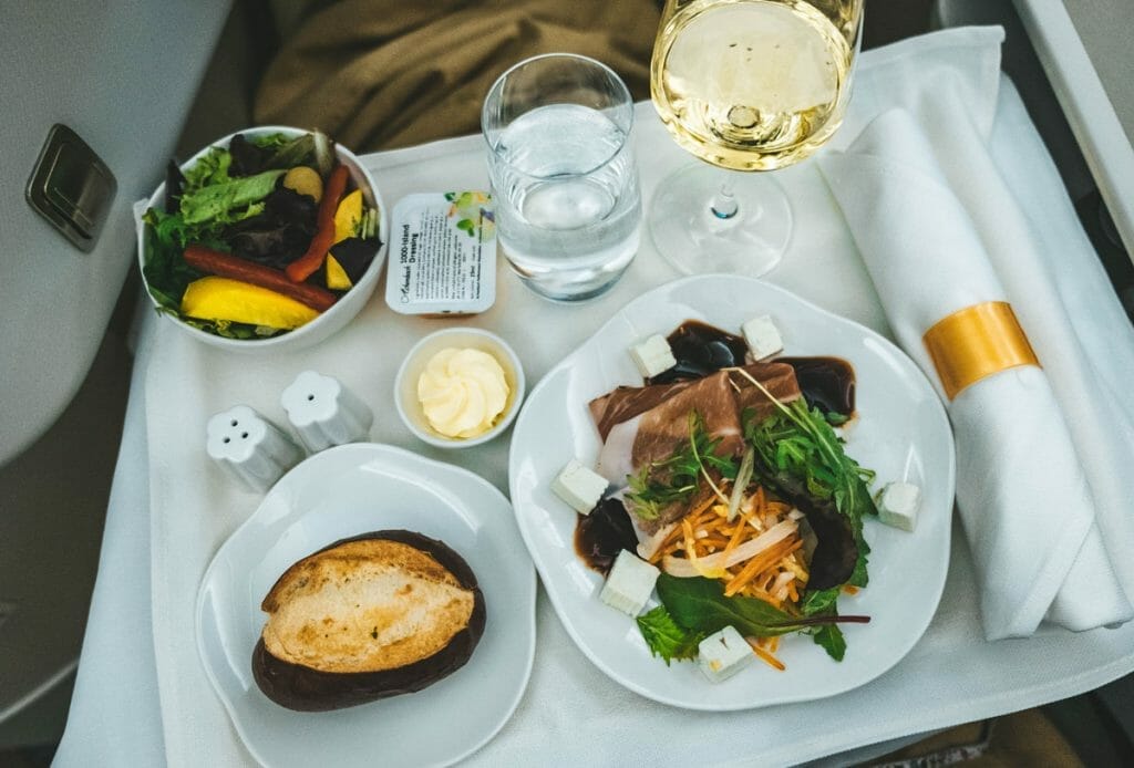 Starter tray with salad, pretzel roll and white wine glass on a plane